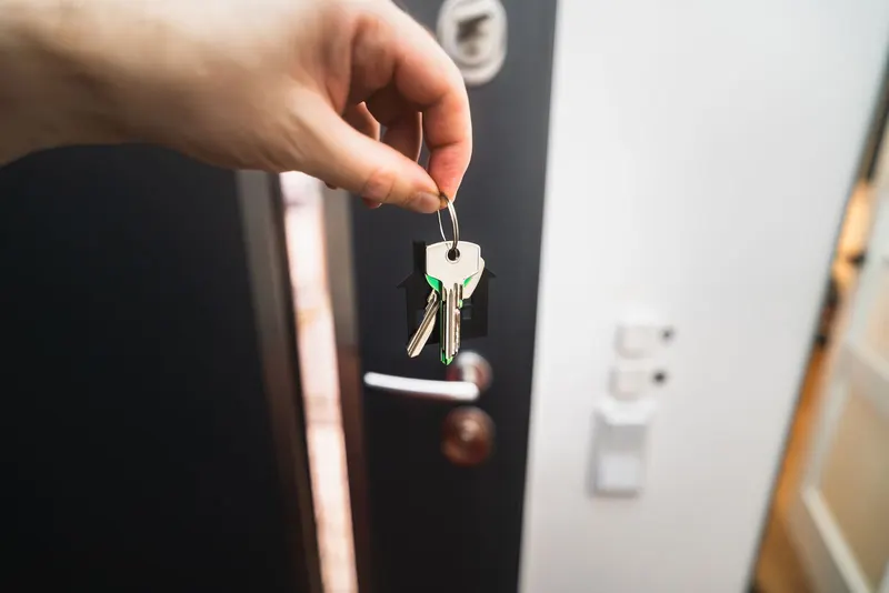 A hand holding house keys in front of an open front door